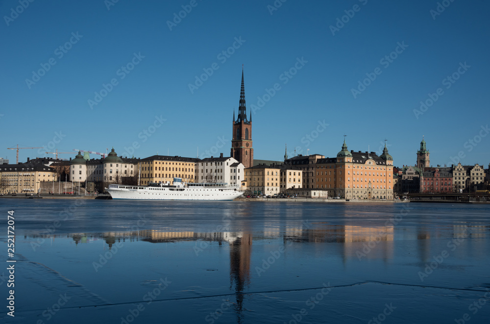 Obraz premium An sunny early spring day in Stockholm, view over a pier with boats and Town City Hall at lake Mälaren