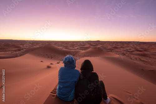 Night landscape with loving couple, boy and girl sitting on the sand dunes looking the horizon . Sunrise in the desert Sahara, Merzouga , Morocco . man and woman . Concept of love photo