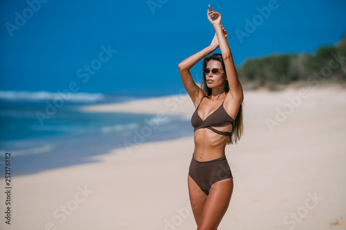 Beautiful tanned girl posing on beach with white sand and blue ocean.
