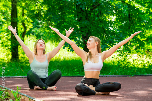 woman and her trainer in the lotus position doing yoga in the park