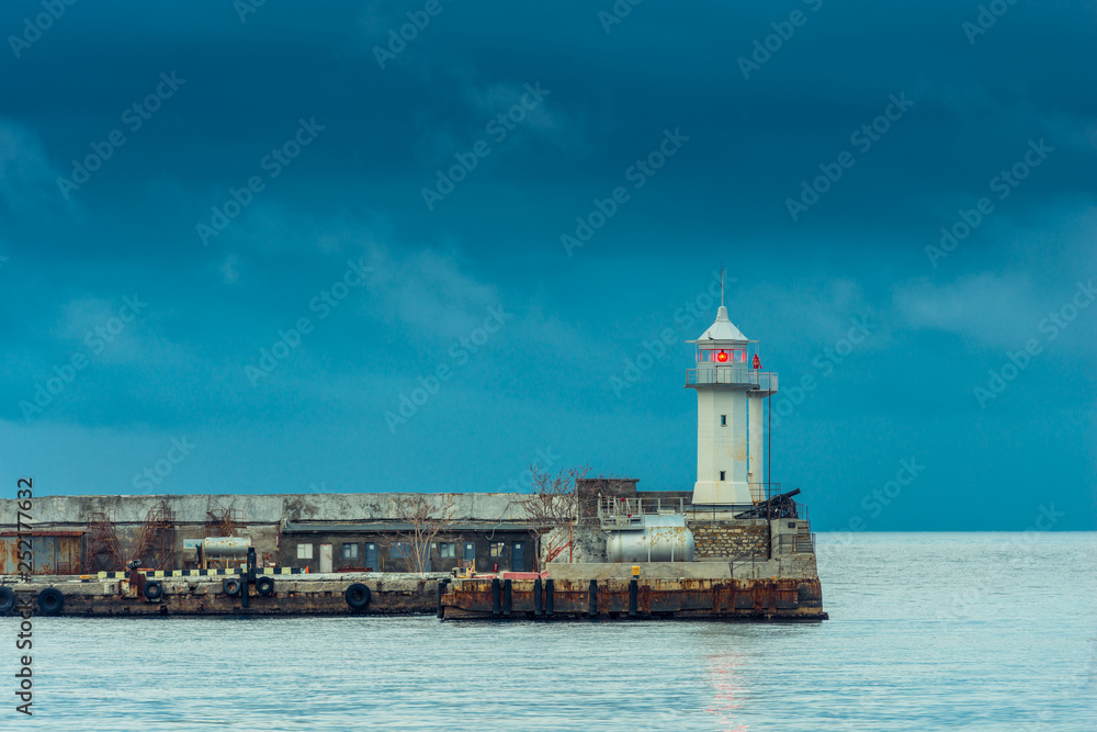Horizontal photo of a lighthouse with a red lantern on the background of the sea and rainy blue clouds