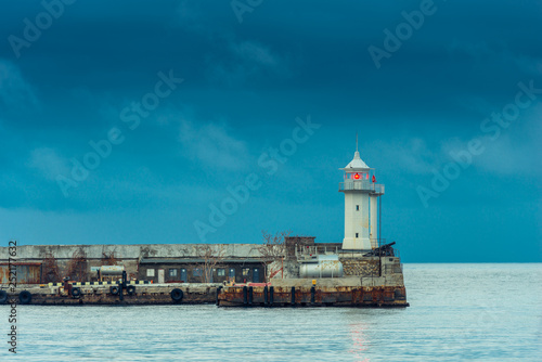 Horizontal photo of a lighthouse with a red lantern on the background of the sea and rainy blue clouds
