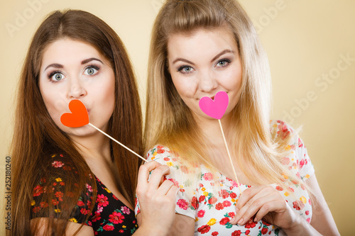 Two happy women holding heart on stick