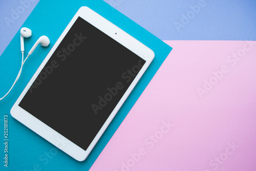 Flat lay of white tablet and earphones on blue, purple and pink background with copyspace.