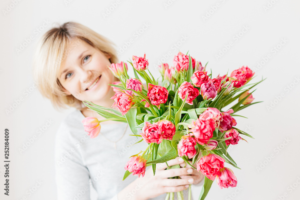 Happy attractive middle-aged blonde woman with a bouquet of red pink white tulips Happy attractive middle-aged blonde woman with a bouquet of red pink white tulips