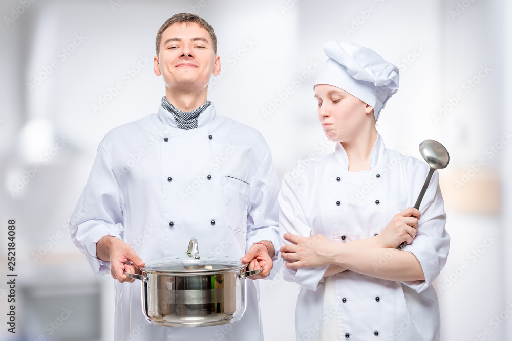 couple in cook costumes posing with a pan on the background of the restaurant's kitchen couple in cook costumes posing with a pan on the background of the restaurant's kitchen