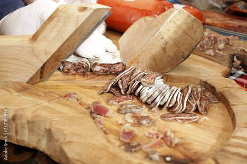  Dry salami on a professional cutting board. Smoked flat sausage with spices for cover photo background. Dried flat salami. Sudzhuk or sudjuk, lukanka. Cut into pieces of sudzhuk made from pork and fa photo