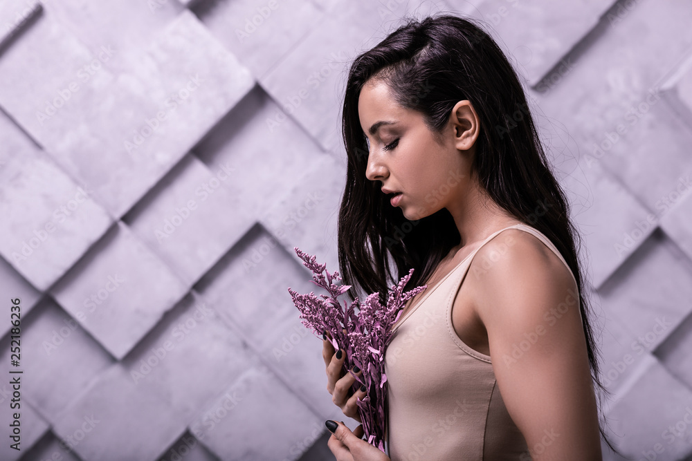 Fototapeta premium Profile studio photo of long-haired brunette girl cuddling lilac flowers