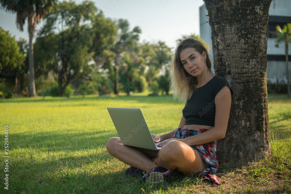 portrait of blonde rests under tree with computer, girl sitting and smiling portrait of blonde rests under tree with computer, girl sitting and smiling