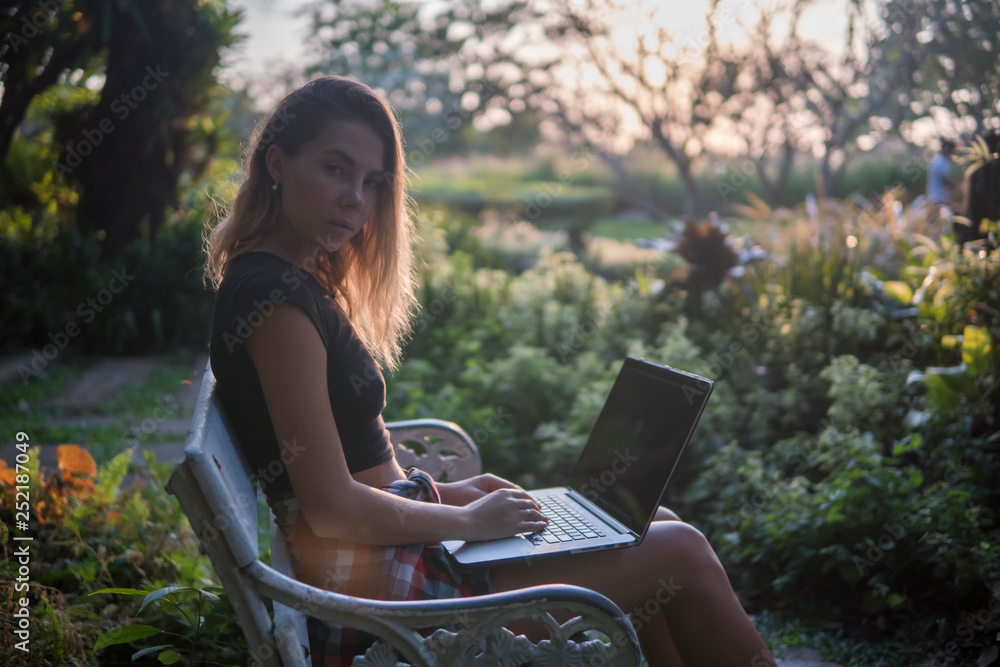 blonde model posing on a park bench with laptop on her knees, looks into camera, blonde model posing on a park bench with laptop on her knees, looks into camera,