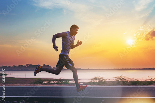 Fototapeta Naklejka Na Ścianę i Meble -  Silhouette of man running sprinting on road. Fit male fitness runner during outdoor workout with sunset background