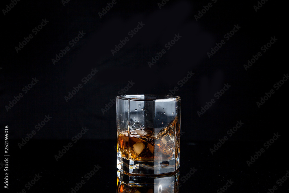 Whiskey splash from the fallen ice cube into glass with beverage isolated on black background..