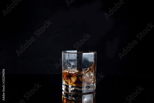 Whiskey splash from the fallen ice cube into glass with beverage isolated on black background..