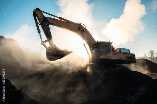 Yellow big excavator in the coal mine, loads the breed, with the bright sun and nice blue sky in the background. Mining truck mining machinery. Technique in coal mine photo