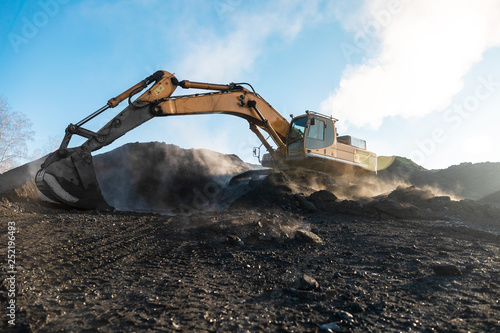 Yellow big excavator in the coal mine, loads the breed, with the bright sun and nice blue sky in the background. Mining truck mining machinery. Technique in coal mine