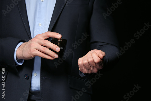 Handsome man with bottle of perfume on dark background, closeup