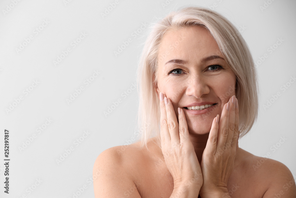 Mature woman giving herself face massage on light background Mature woman giving herself face massage on light background