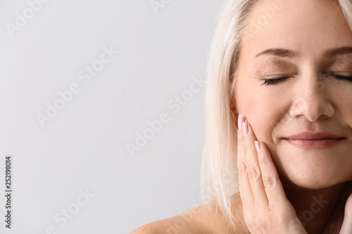 Mature woman giving herself face massage on light background