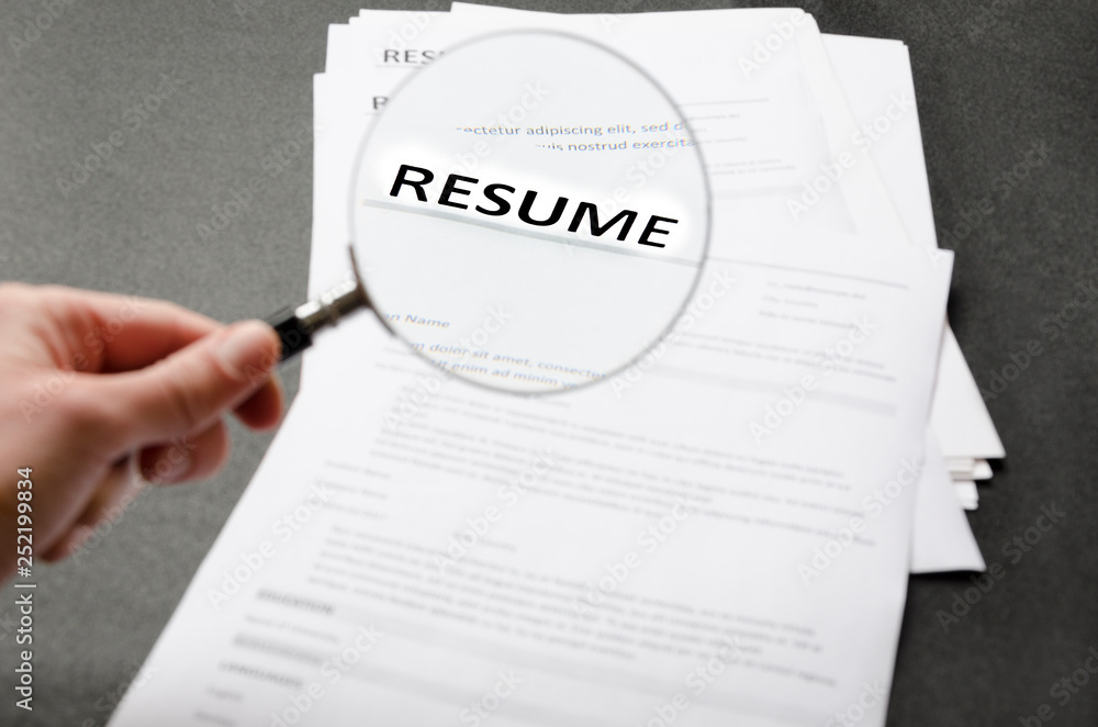 Recruiter`s workplace, pile of resume examples,hand holding magnifier,Concept of analyzing information about new employees Recruiter`s workplace, pile of resume examples,hand holding magnifier,Concept of analyzing information about new employees