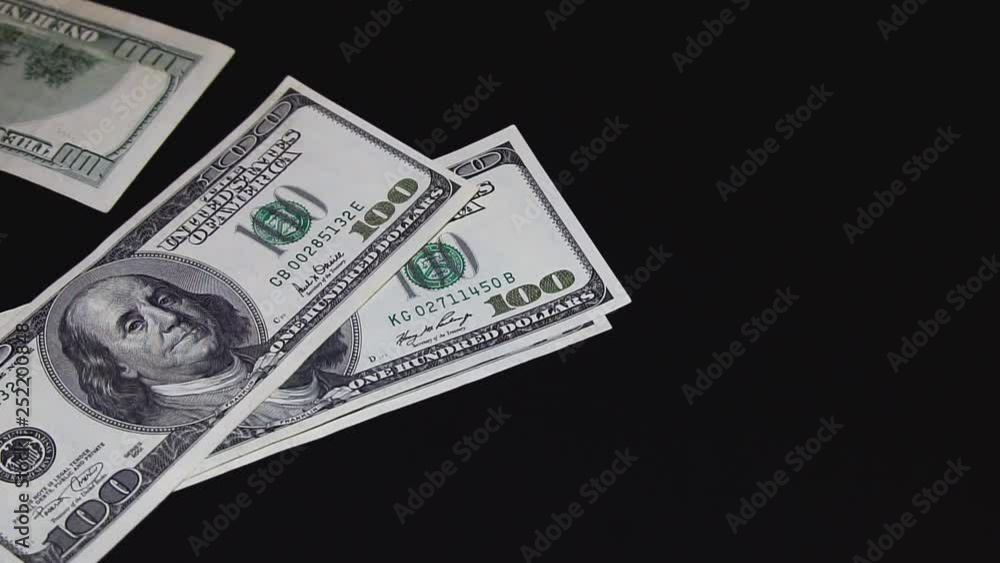 TOP VIEW: Many US dollars lie down, fly, rush to the black table. A man throws dollars on the table. Slow motion.