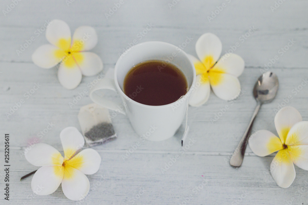 cup of dark tea on wooden table with spoon and flowers all around