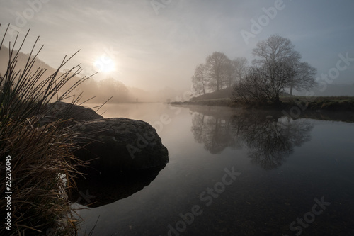 Sunrise on a misty morning over the River Brathay, between Elterwater and Skelwith Bridge. Trees reflected in the water. Lake District, UK photo