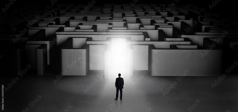Lost businessman standing at the dark labyrinth with illuminated door
Lost businessman standing at the dark labyrinth with illuminated door