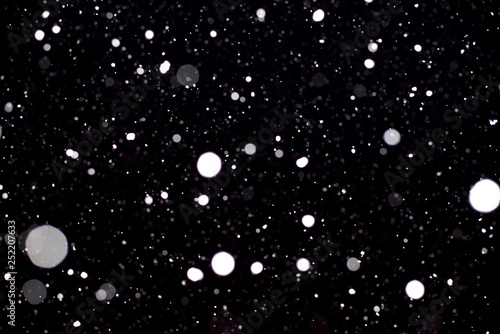 Large flakes of snow against the black sky, swirling in the light of lantern. - Image