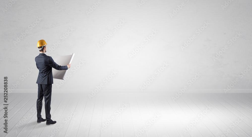 Young architect with construction helmet standing in an empty space and holding a plan
Young architect with construction helmet standing in an empty space and holding a plan