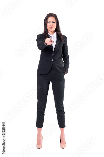 Authoritative female business manager pointing finger at you looking at camera with forced smile. Full body isolated on white background. 