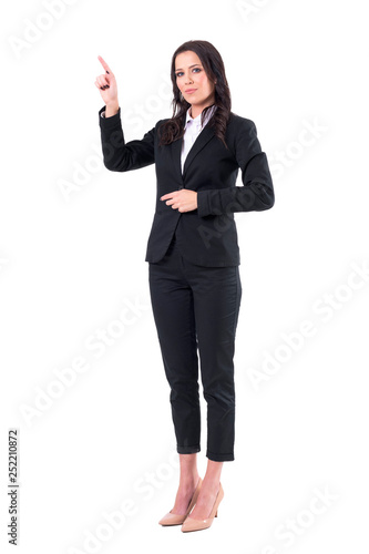 Young pretty confident business woman pointing finger at copyspace. Full body isolated on white background. 