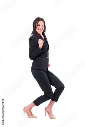 Ecstatic business woman in suit crouching with clenched fist celebrating success. Full body isolated on white background. 
