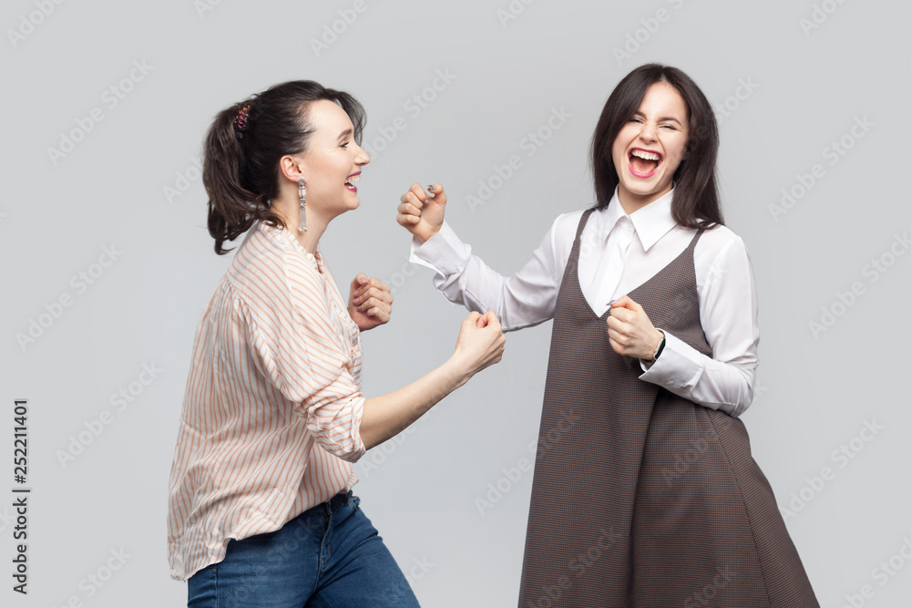 Portrait of two happy beautiful brunette best friends in casual style standing and having fun together and celebraiting their victory. indoor studio shot, isolated on grey background. Portrait of two happy beautiful brunette best friends in casual style standing and having fun together and celebraiting their victory. indoor studio shot, isolated on grey background.