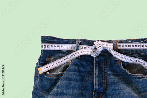 Jeans with a measuring tape on a green background. Weight loss concept photo