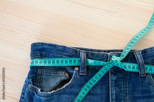 Jeans with a measuring tape on a green background. Weight loss concept photo