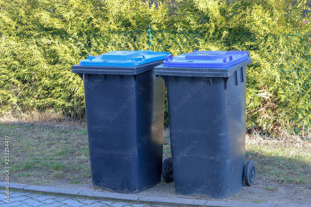 Two garbage cans or trash cans on the road in front of a green hedge Stock  Photo