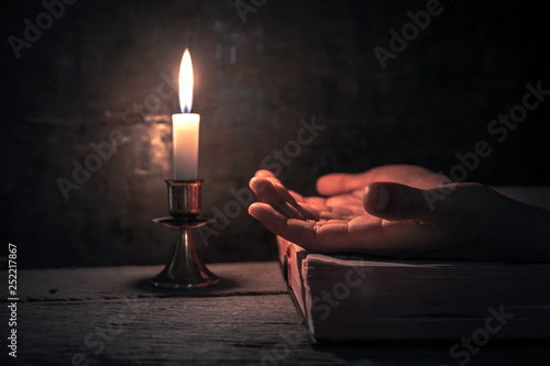 Close up hands praying on bible with light of candle on wooden table at worship room. christian concept.