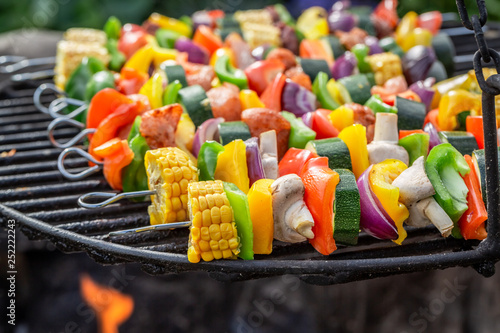 Tasty skewers on grill with vegetables and meat