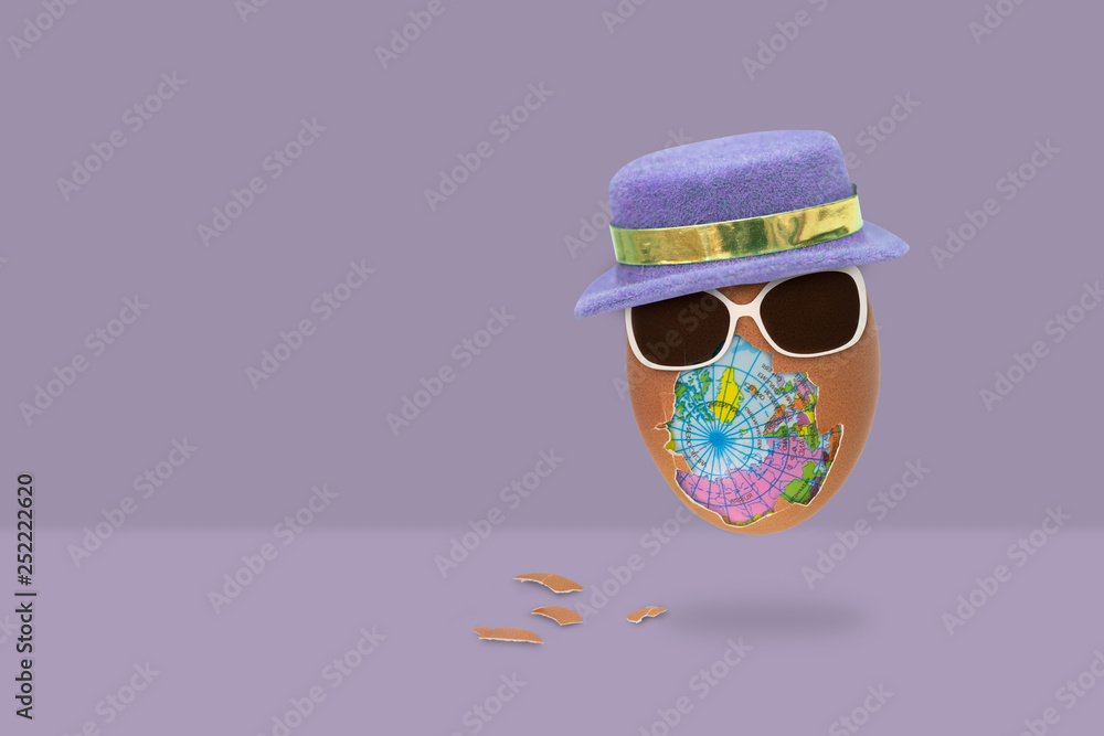 Fototapeta premium The shelled egg has an globe inside with glasses and hat is flying on purple background.