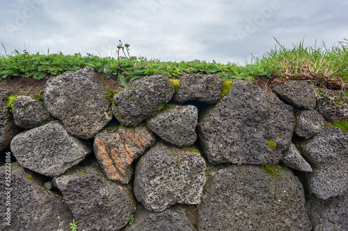 Stone fence covered with grass against the sky