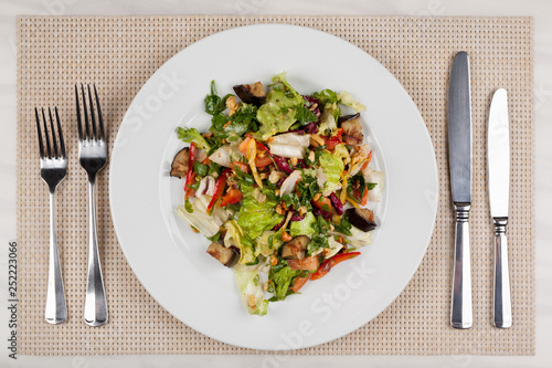 Eggplant salad with vegetables and walnuts and cutlery on a white plate.