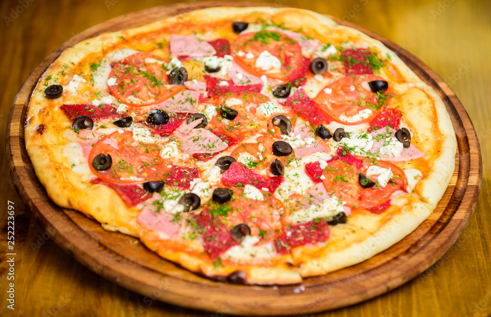 Pizza served with dill. Delicious hot pizza on wooden board plate. Food delivery service. Pizza with tomatoes black olives and ham. Take away food concept. Pizzeria restaurant. Italian pizza concept