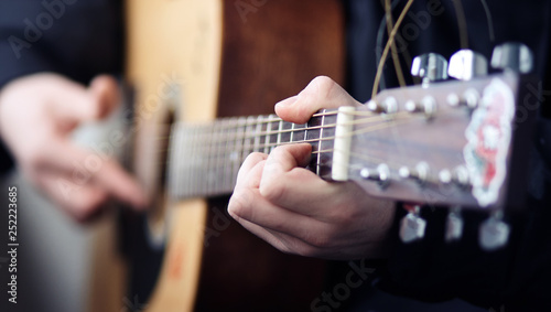 A man in black clothes playing a rock song on a beautiful wooden acoustic guitar, clamping chords