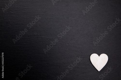 Weißes Herz aus Holz auf dunkler Steinplatte