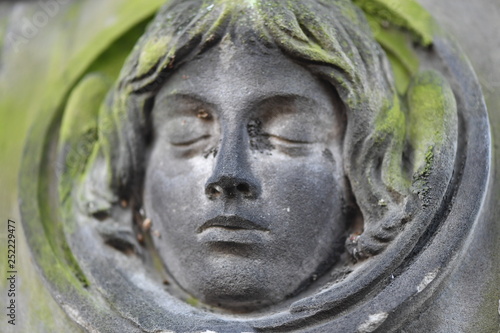 An old, moss covered sandstone sculpture of a female face. 