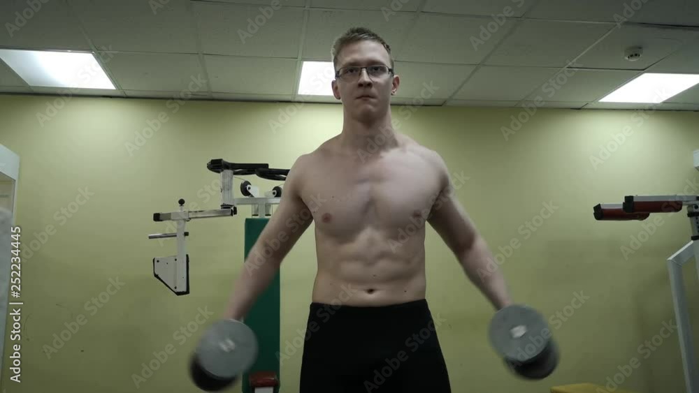 A young man trains his shoulders with dumbbells in the gym A young man trains his shoulders with dumbbells in the gym