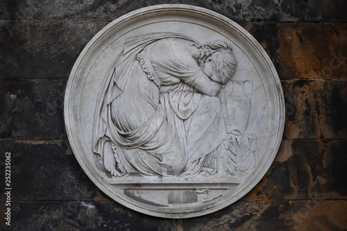 An old, weathered sandstone relief of grieving mother in front of a crypt in Berlin-Germany.