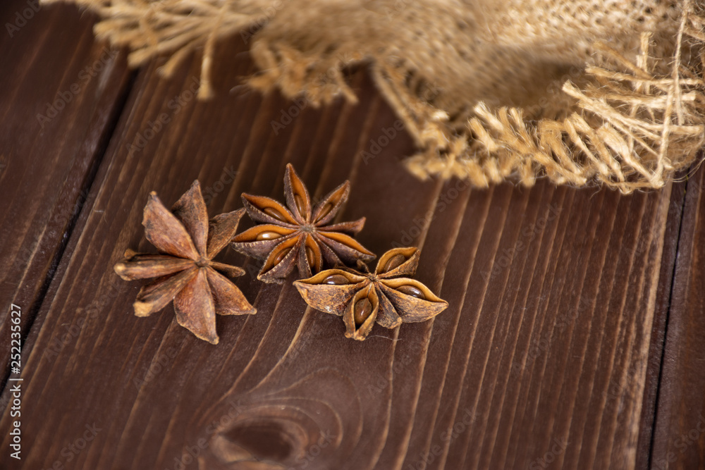Group of three whole dry brown star anise fruit in a focus on jute cloth on brown wood