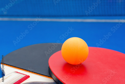 pingpong rackets and ball and net on a blue pingpong table