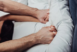 cropped view of couple holding hands and lying in bed at home